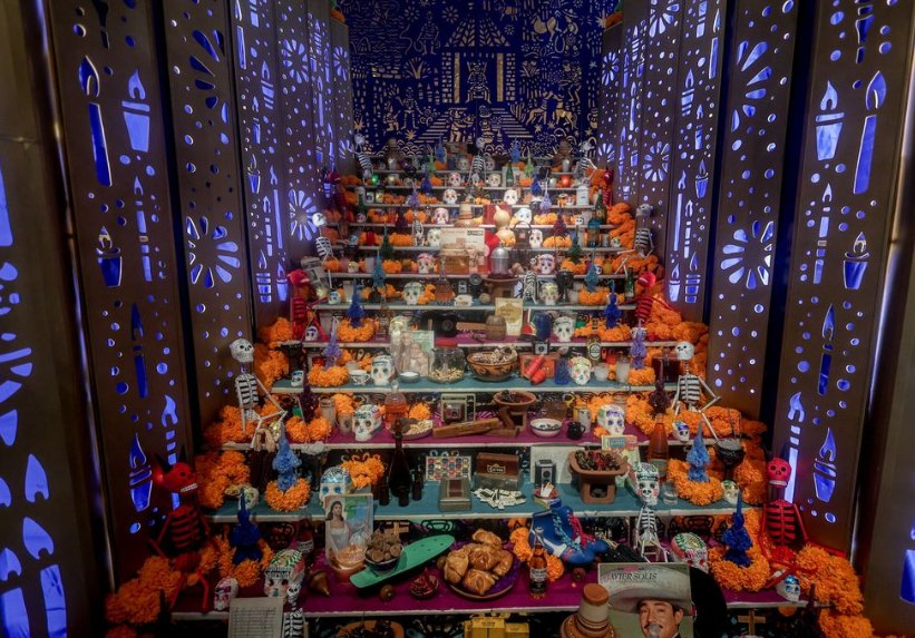 A tiered Day of the Dead altar with marigolds, sugar skulls and offerings between walls of lit candle cutouts